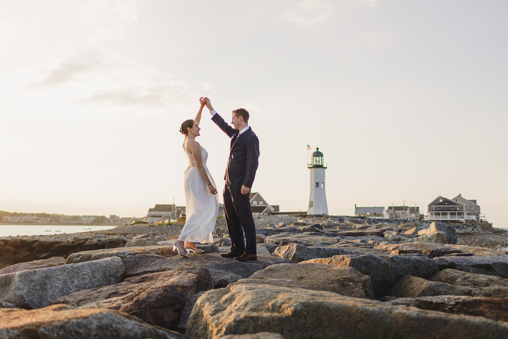 Couple dressed in wedding clothes dancing on the jetty at Scituate Lighthouse at sunset