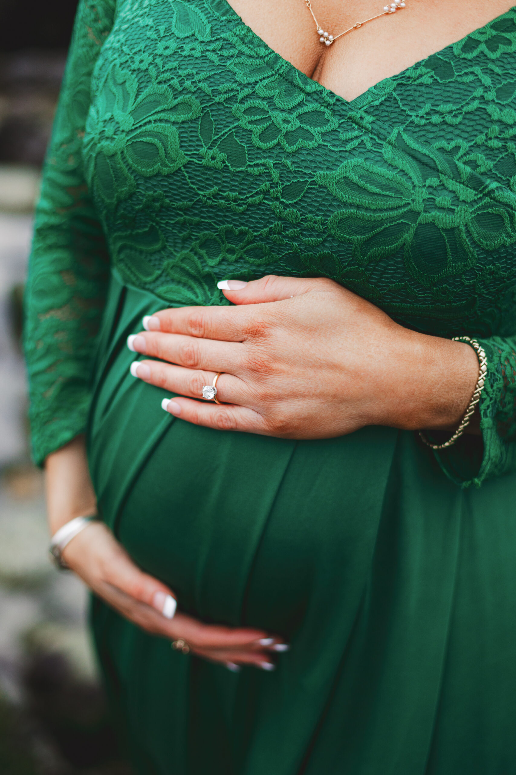 Photo of pregnant woman in green dress with hands on belly at Whitehorse Beach in Plymouth