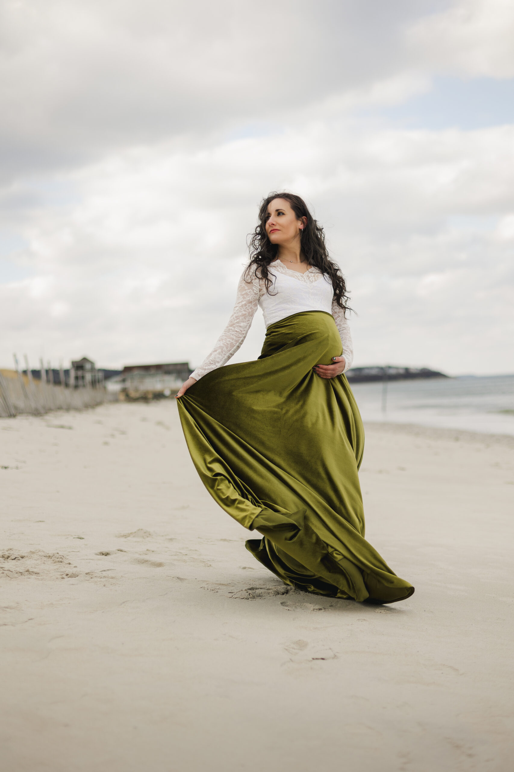 Pregnant woman in long green skirt posing at White Horse Beach in Plymouth for maternity photo